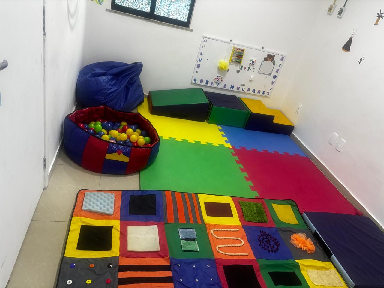 Sala de integração sensorial com piscina de bolinhas, tapete de texturas e tatame colorido